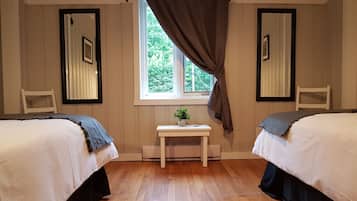 A room with two beds, a window with curtains, a small table with a plant, and two chairs.