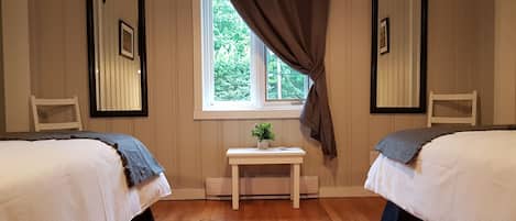 Een kamer met twee bedden, een raam met gordijnen, een tafeltje met een plant en twee stoelen.
