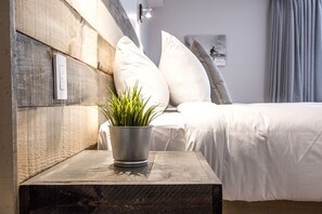 A modern bedroom with a wooden headboard, a bedside table with a potted plant, and a bed with white bedding. - Hotel Far Hills (Val Morin)