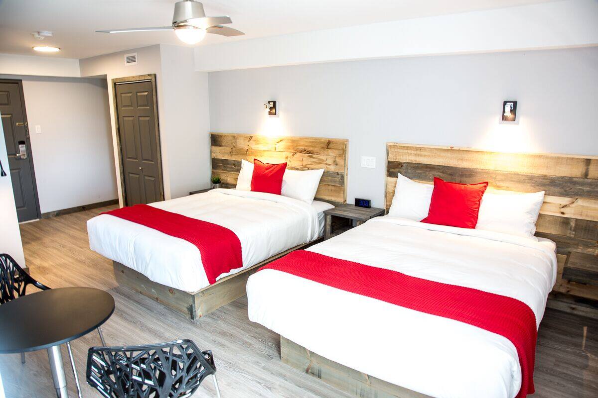 A hotel room with two beds, each with a wooden headboard and red and white bedding. There is a small table and a chair in the room.