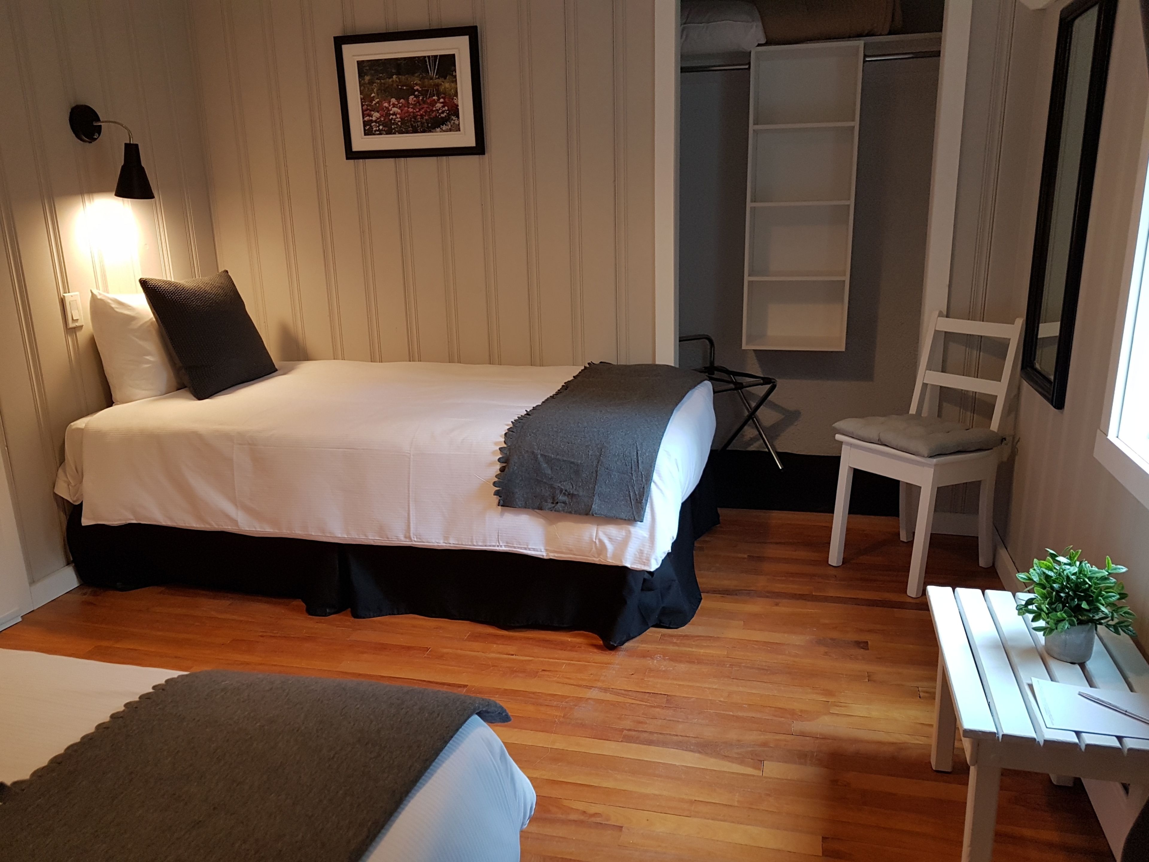 A bedroom with a bed, bedside table, chair, and a small table with a plant.