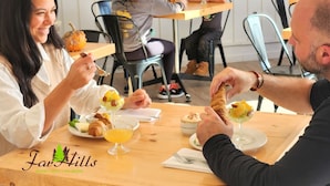 Un comedor con mesas y sillas de madera, personas comiendo y un cartel que dice 'Fav Hills Resort Hotel Val Morin'.