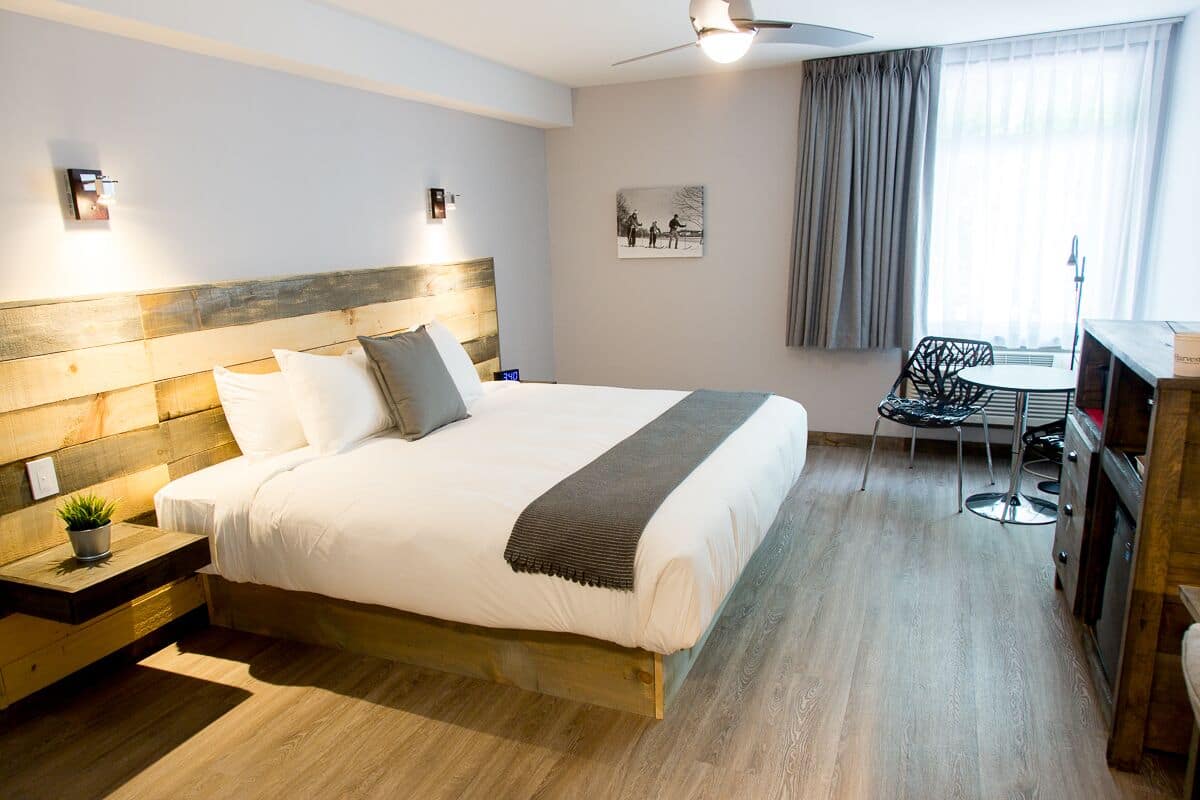 A neatly arranged hotel room with a large bed, bedside tables, a small desk, a chair, and a window with curtains.