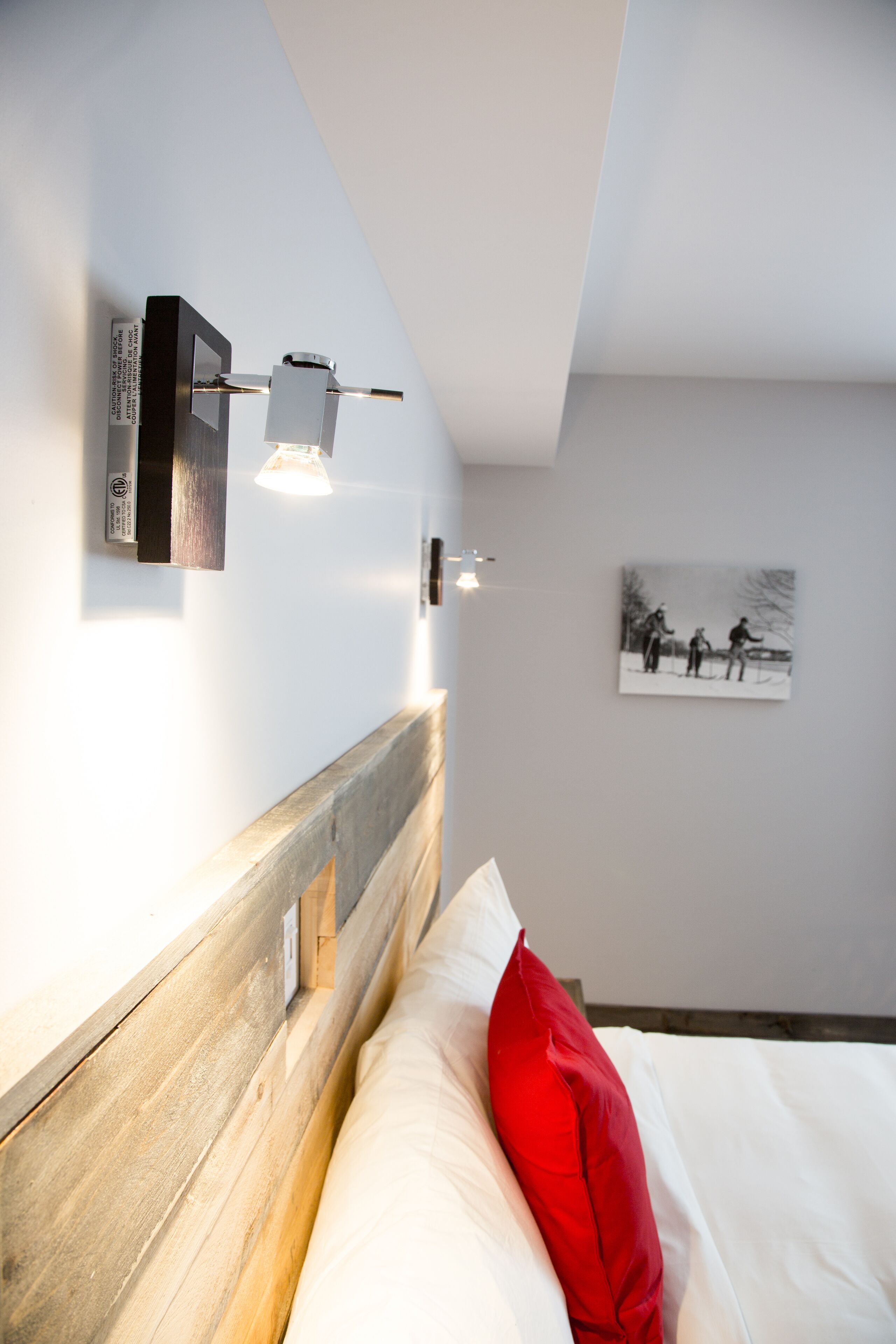 Ein modernes Hotelzimmer mit einem Holzkopfteil, einem roten Kopfkissen und einem Schwarz-Weiß-Foto an der Wand.