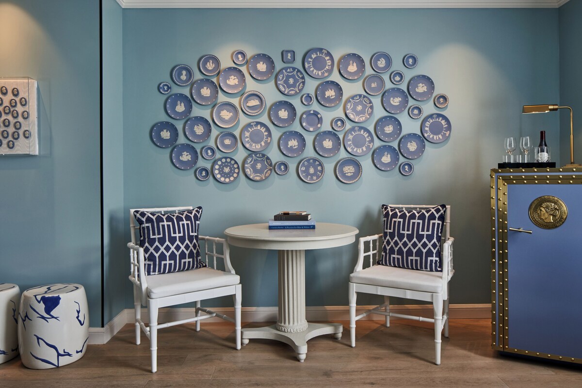 A room with two white chairs, a round table, and a wall decorated with numerous blue and white plates.