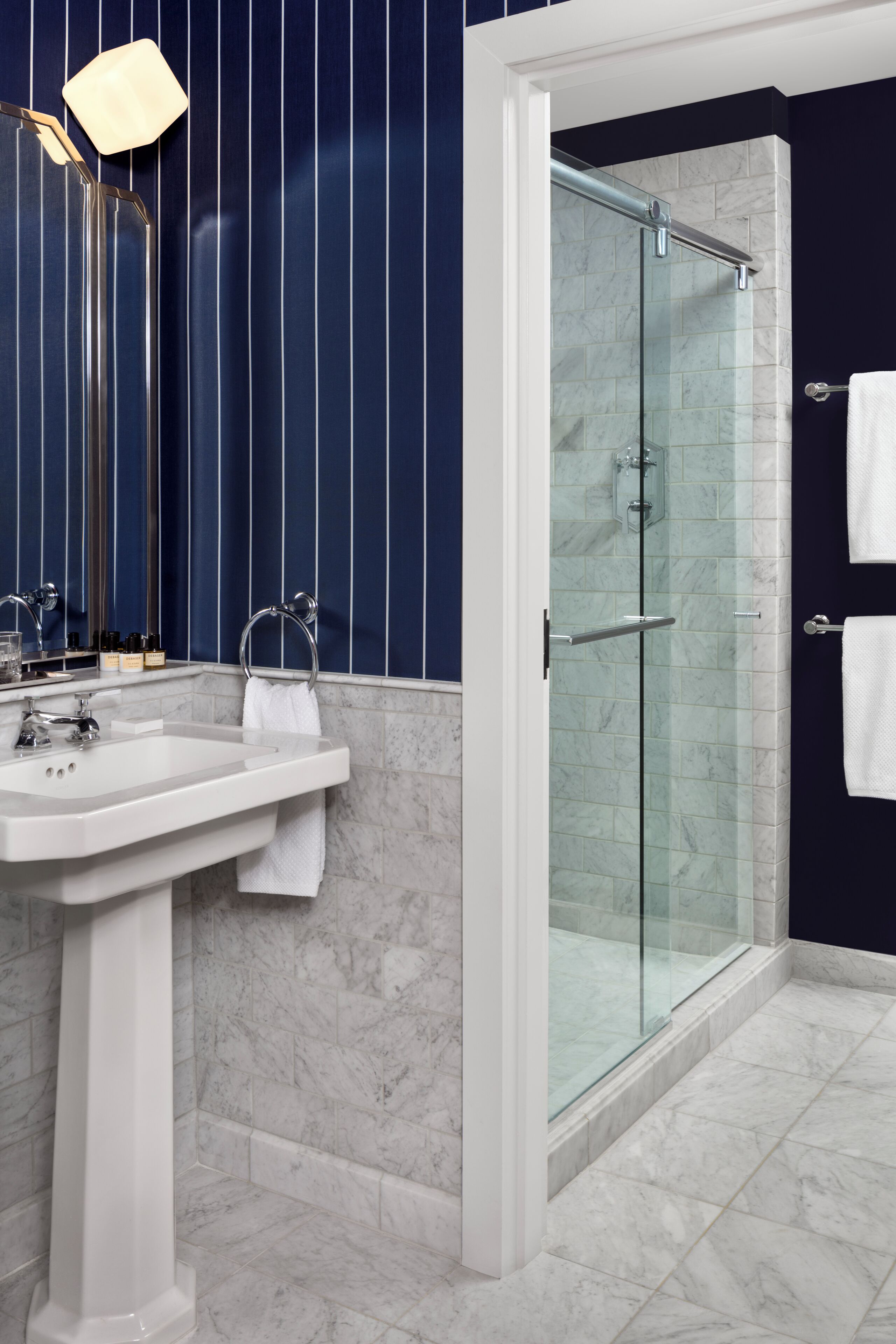 Un baño con ducha de vidrio, lavamanos con espejo y perchero para toallas.