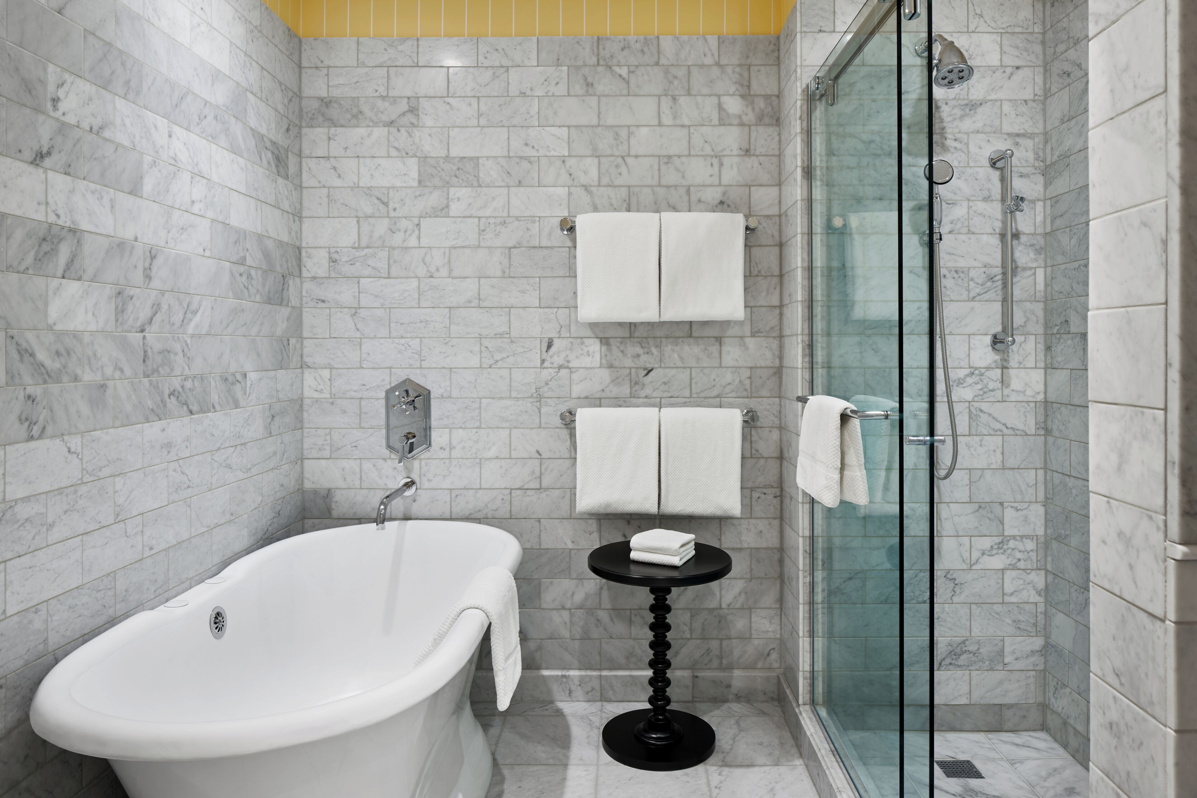 A bathroom with a freestanding bathtub, a glass-enclosed shower, and a small round table with a towel.