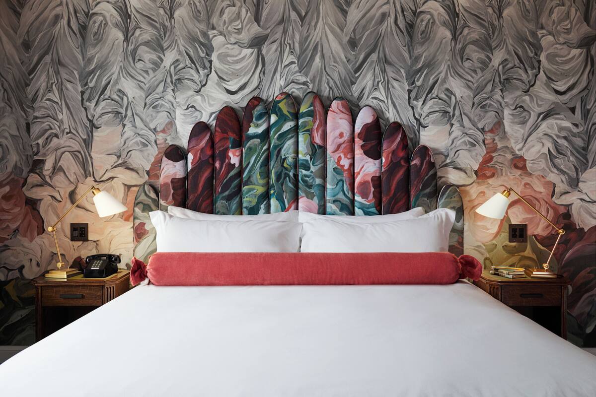 Una cama bien hecha con ropa de cama blanca y roja, dos mesitas de noche con lámparas y un papel tapiz con motivos florales.