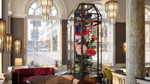 A spacious lobby with a red sofa, a patterned armchair, and a glass display case with flowers.