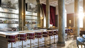 A bar area with marble columns, bar stools, and a well-stocked liquor shelf.