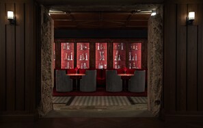 A dimly lit room with a red-tinted glass display case filled with trophies, a red carpet, and grey upholstered chairs.