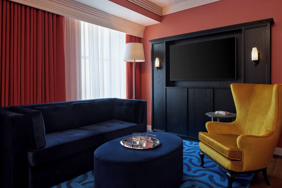 Una sala moderna con un sofá azul oscuro, un sillón amarillo y un taburete redondo con una bandeja.
