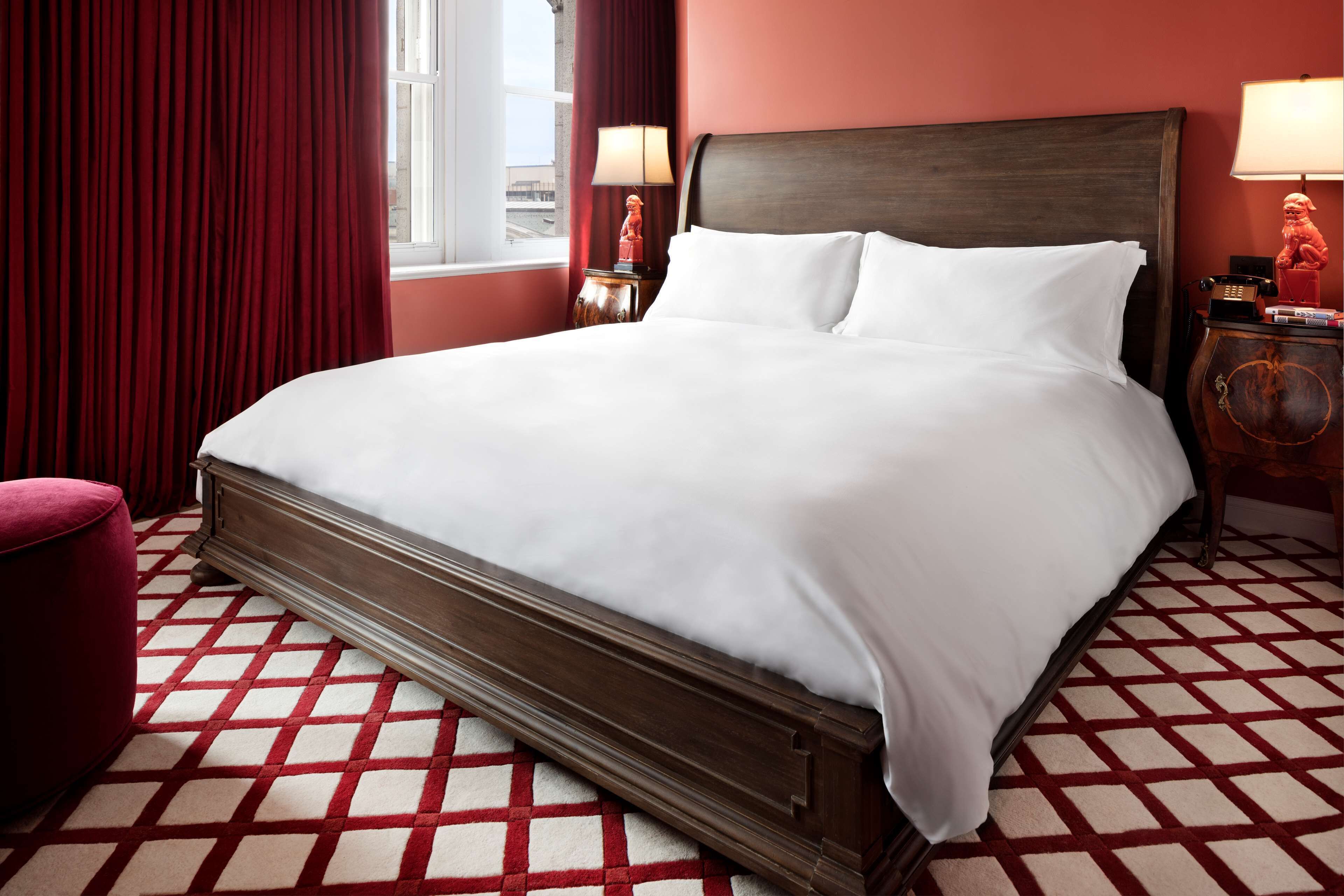 Una cama grande con sábanas blancas en una habitación con piso a cuadros rojo y blanco.