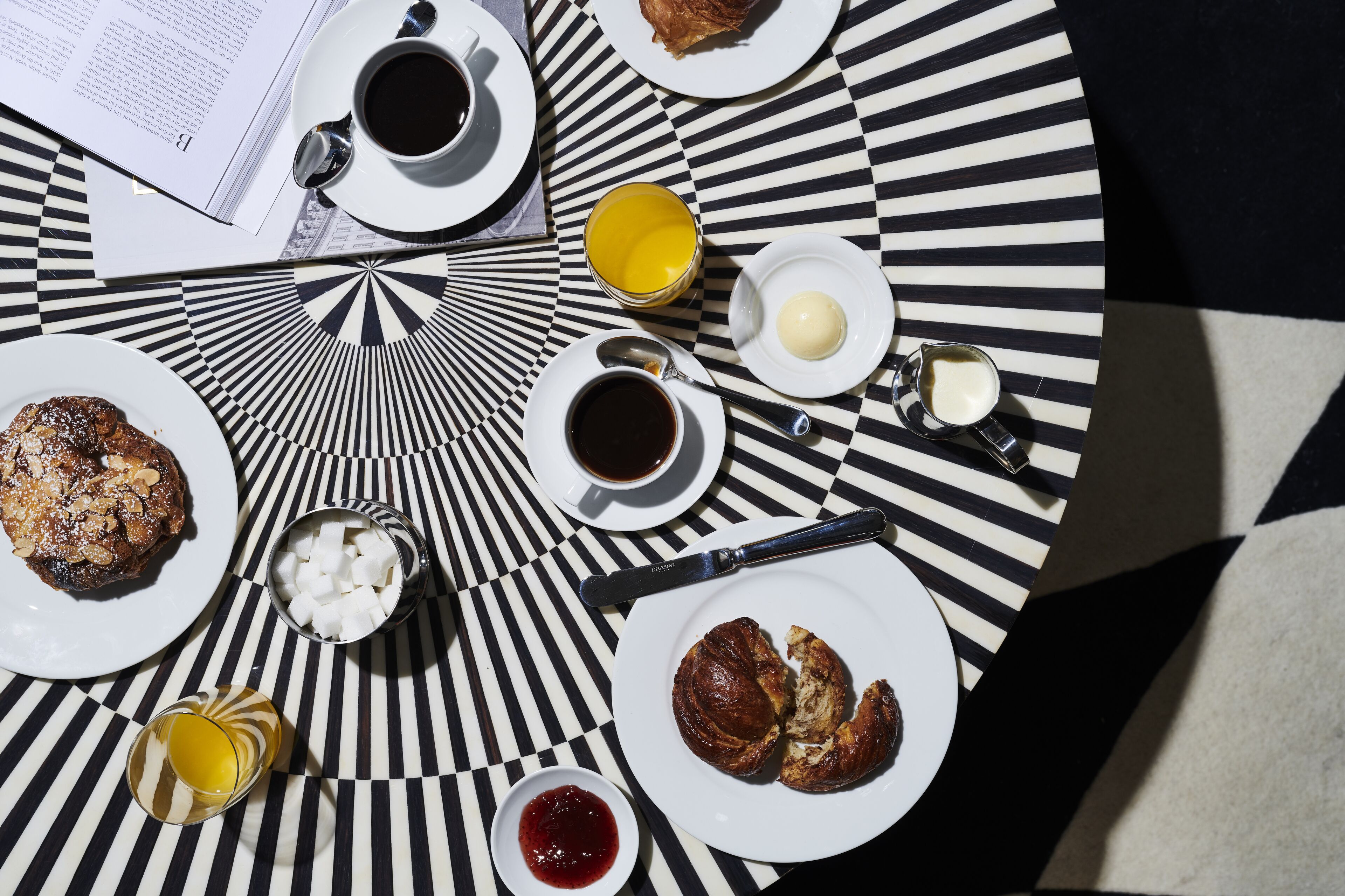 Mesa com itens de café da manhã, incluindo doces, café e suco, sobre uma toalha xadrez.