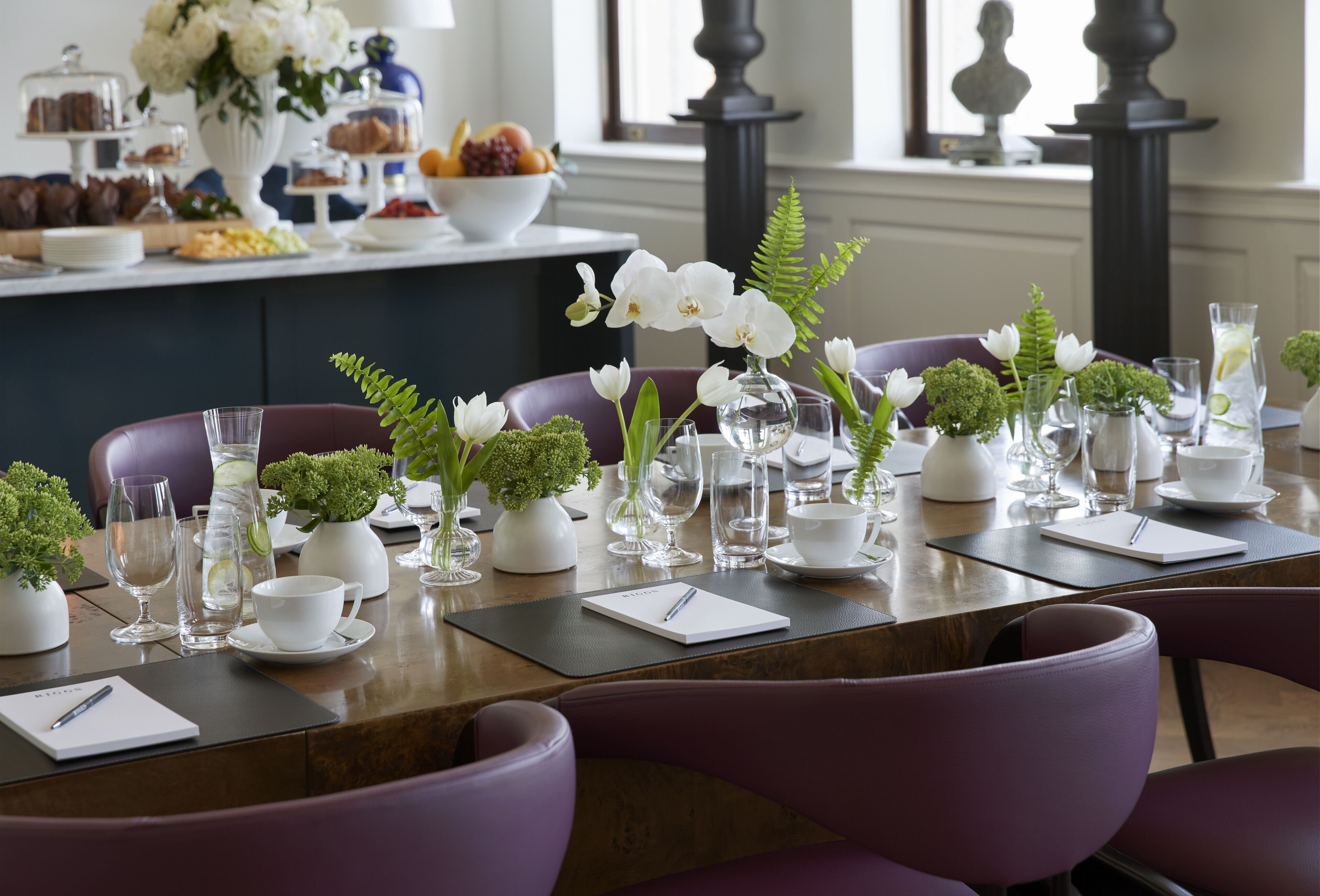 A dining table set with white plates, cups, and a notepad, surrounded by purple chairs.
