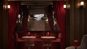 A room with a red sofa, two round tables, and a red lamp.