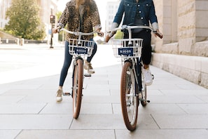 Two bicycles with baskets labeled "RIGGS" on a paved sidewalk.