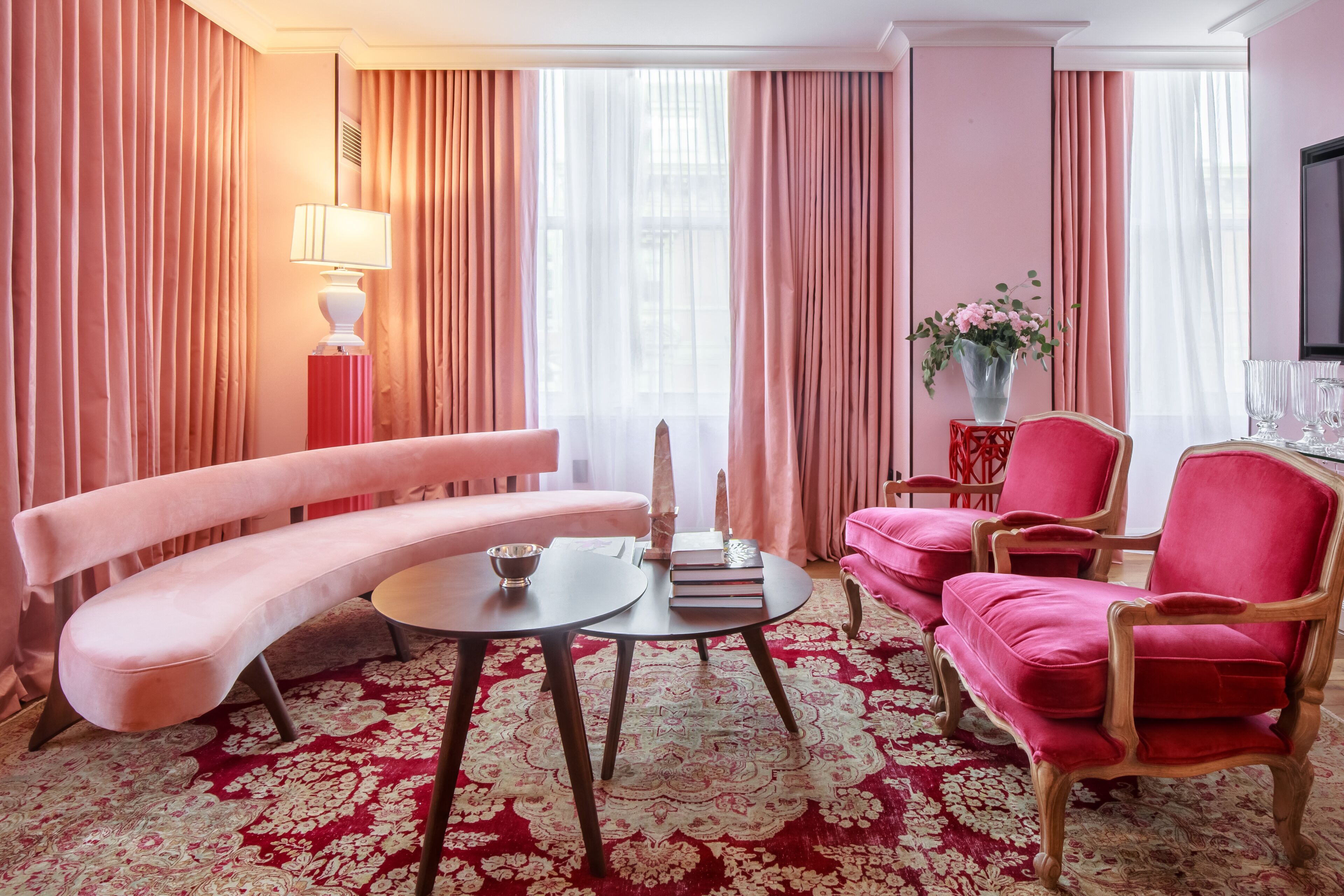 Una habitación con sofá, sillón, mesa, lámpara y un florero con flores.