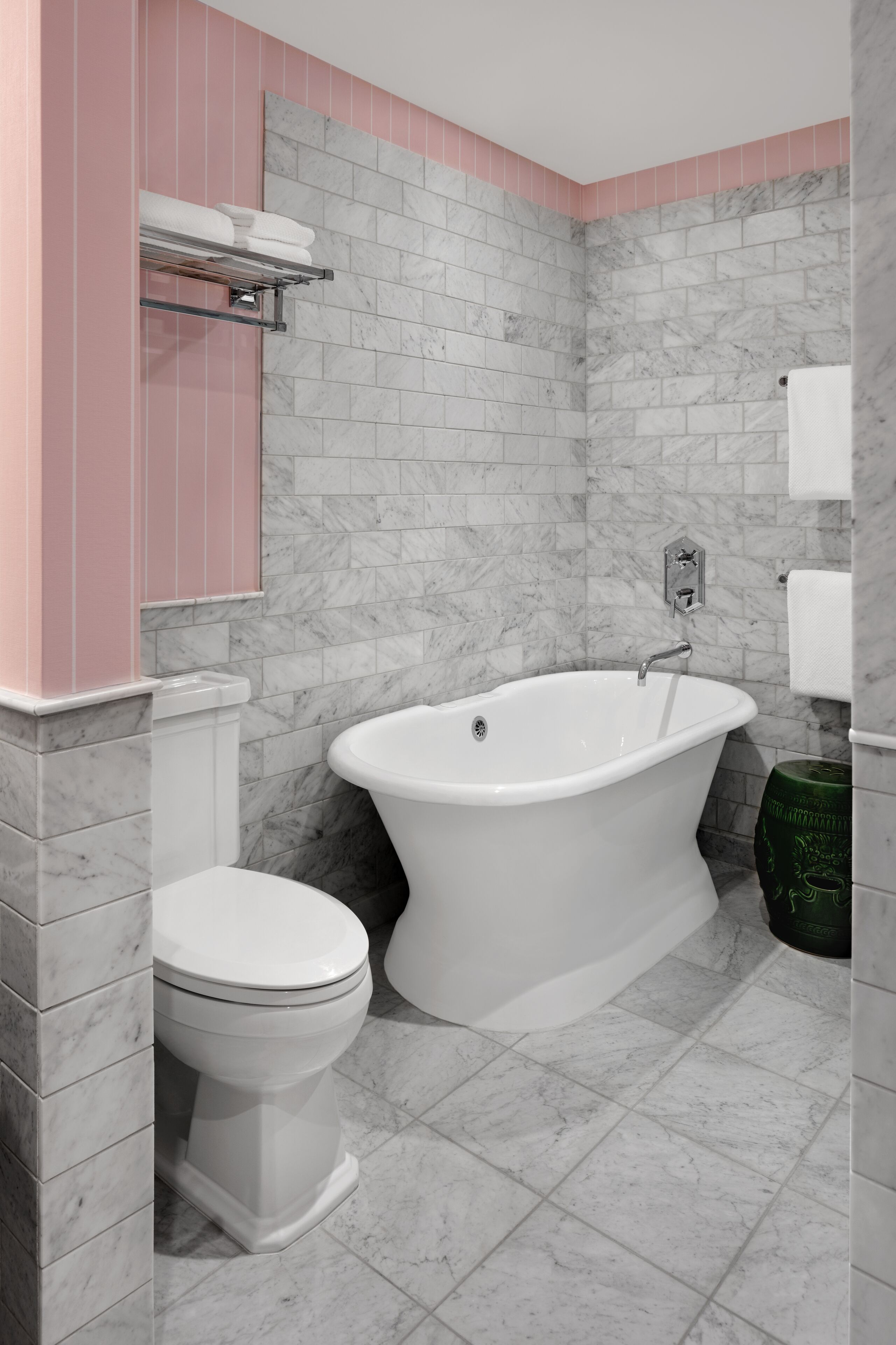A bathroom with a white bathtub, a toilet, and a marble-tiled wall.