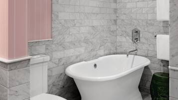 A bathroom with a white bathtub, a toilet, and a marble-tiled wall.