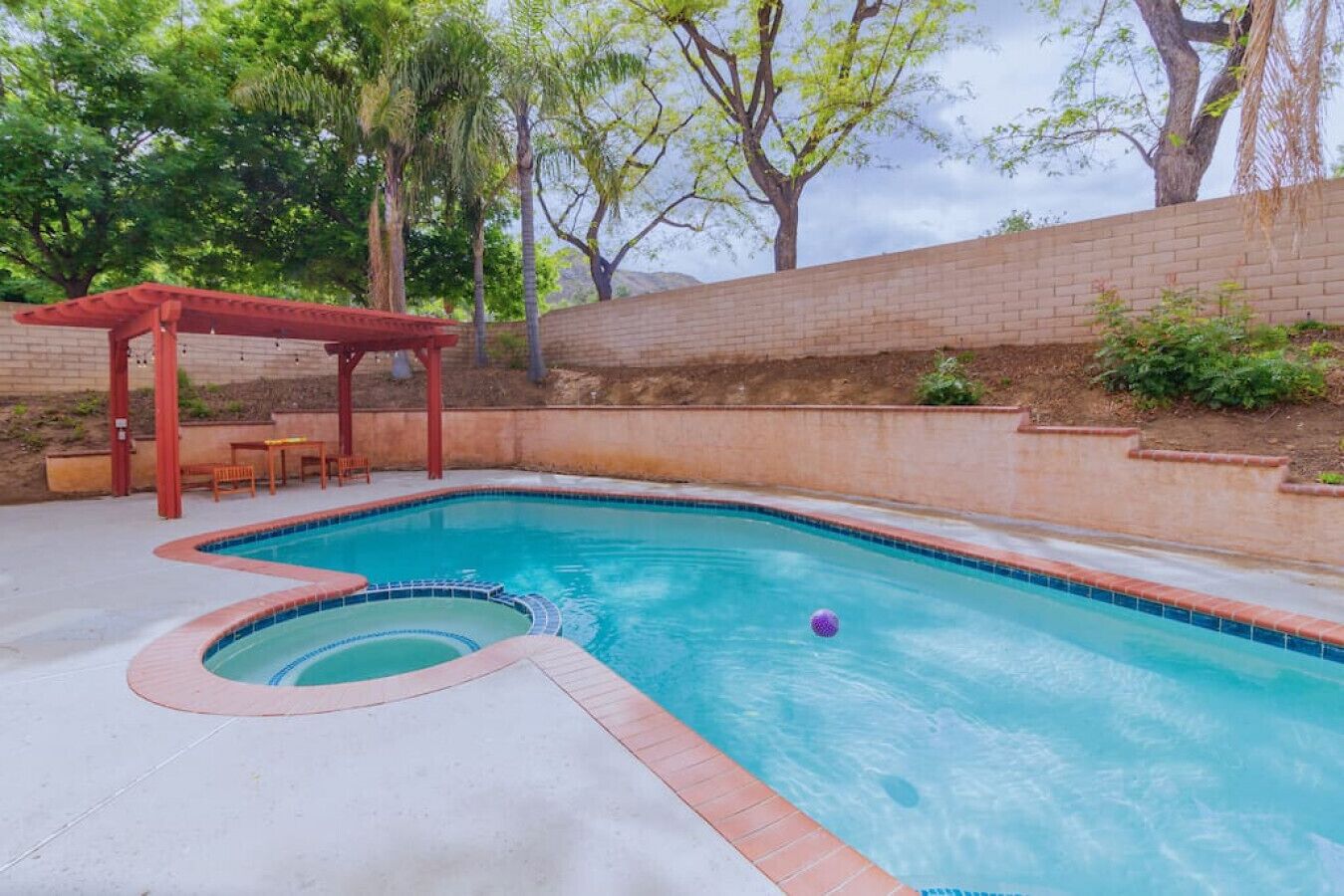 A swimming pool with a red pergola and a brick wall.