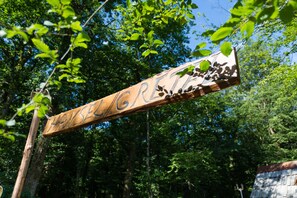 A wooden sign with the name "HANSEN" carved into it, set against a backdrop of lush green trees and a clear blue sky.