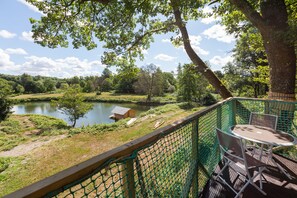 A view from a green-roofed deck overlooking a lake, with a small wooden structure and a table with chairs.