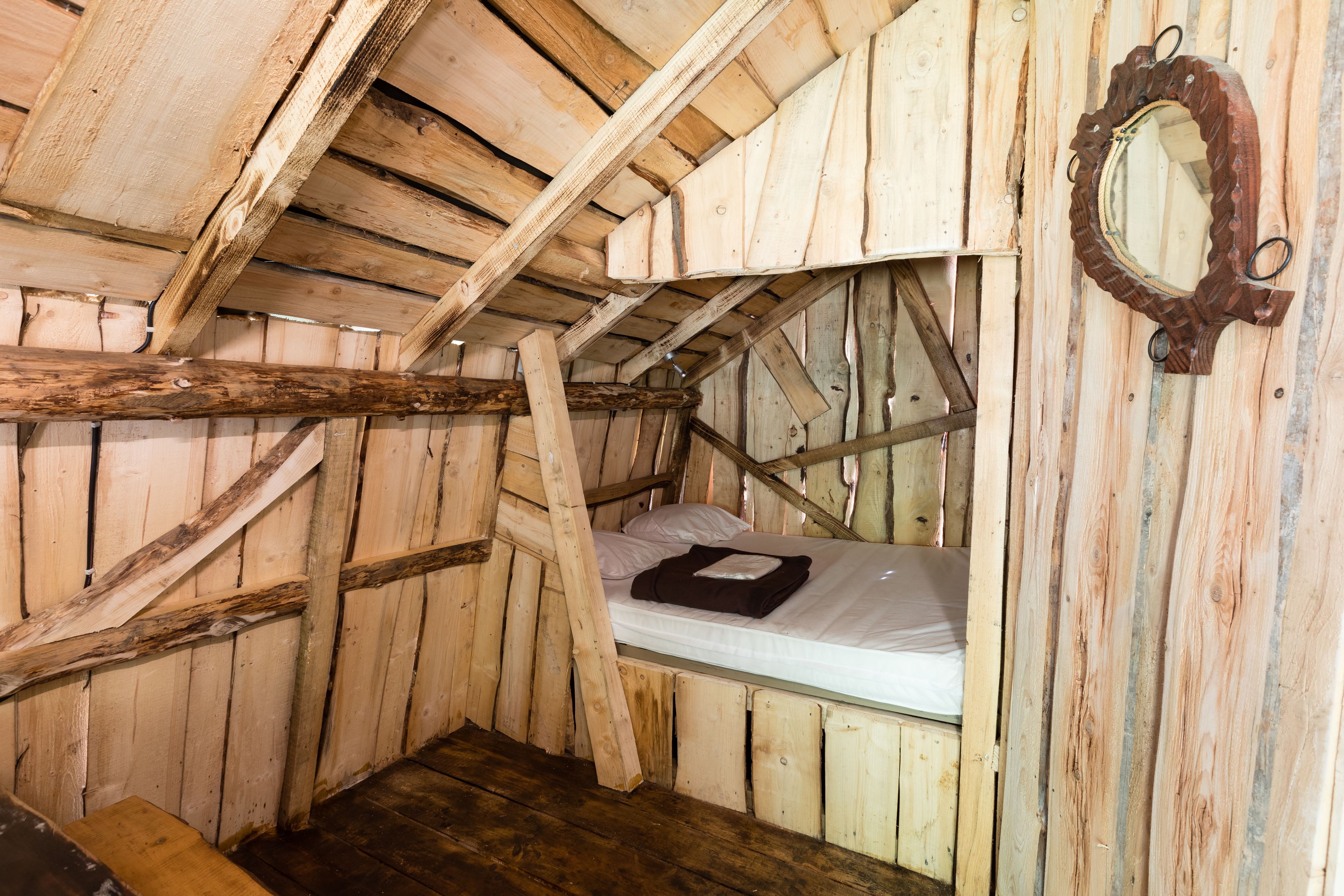 Een rustieke houten kamer met een videbed, een houten ladder en een spiegel met houten lijst.