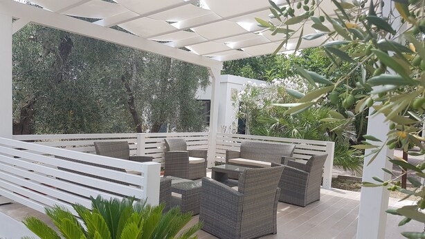 An outdoor patio with wicker furniture, a white pergola, and lush greenery. - Residence Alba (Vieste)
