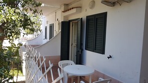 A white building with green shutters, a small white table, and two white chairs outside. - Residence Alba (Vieste)