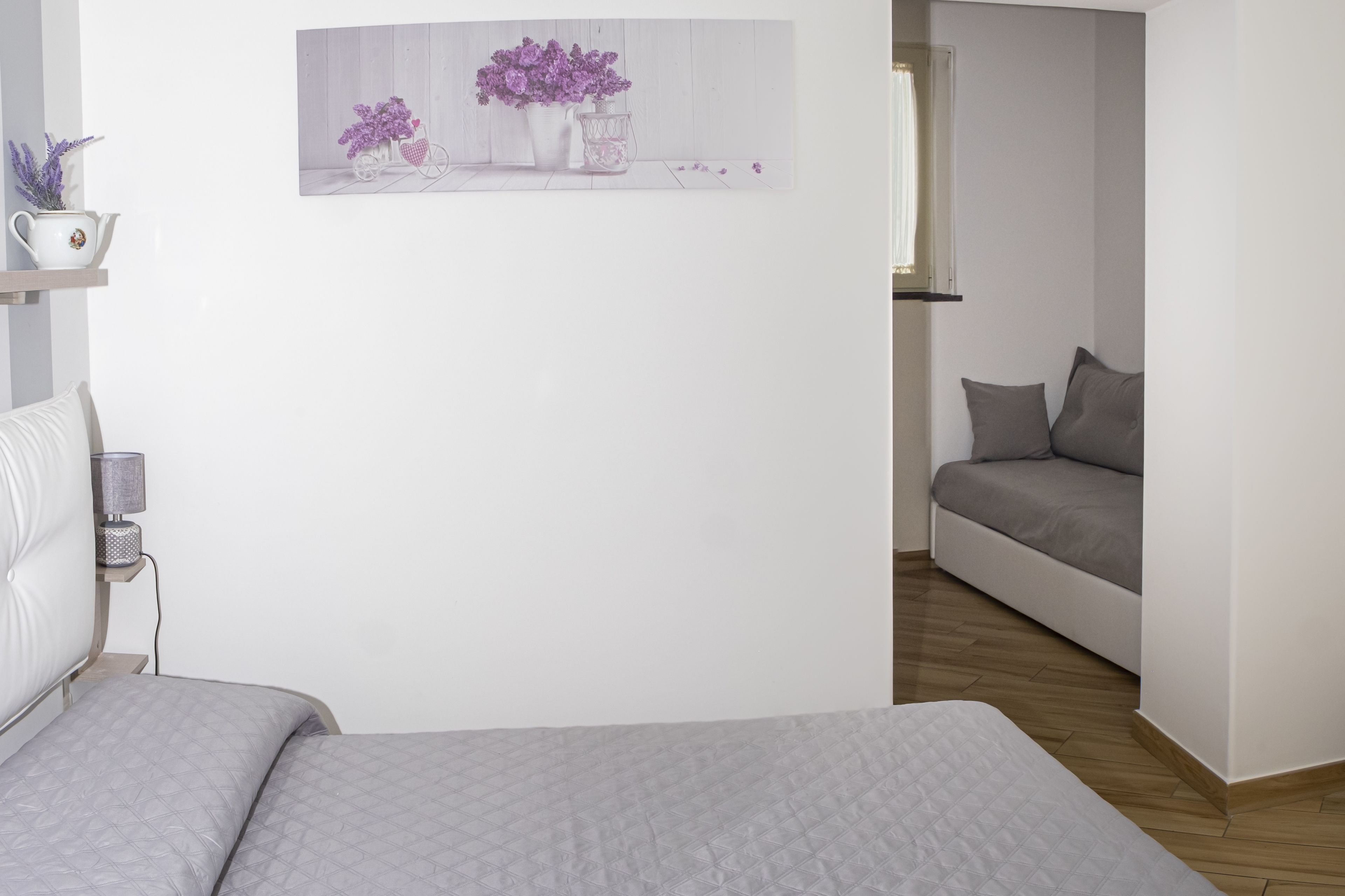 A modern bedroom with a bed, a bedside table with a lamp, and a wall-mounted picture of flowers.