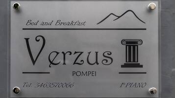 A sign for a hotel named "Verzus" offering bed and breakfast services, located in Pompei. It includes a telephone number and mentions a piano.