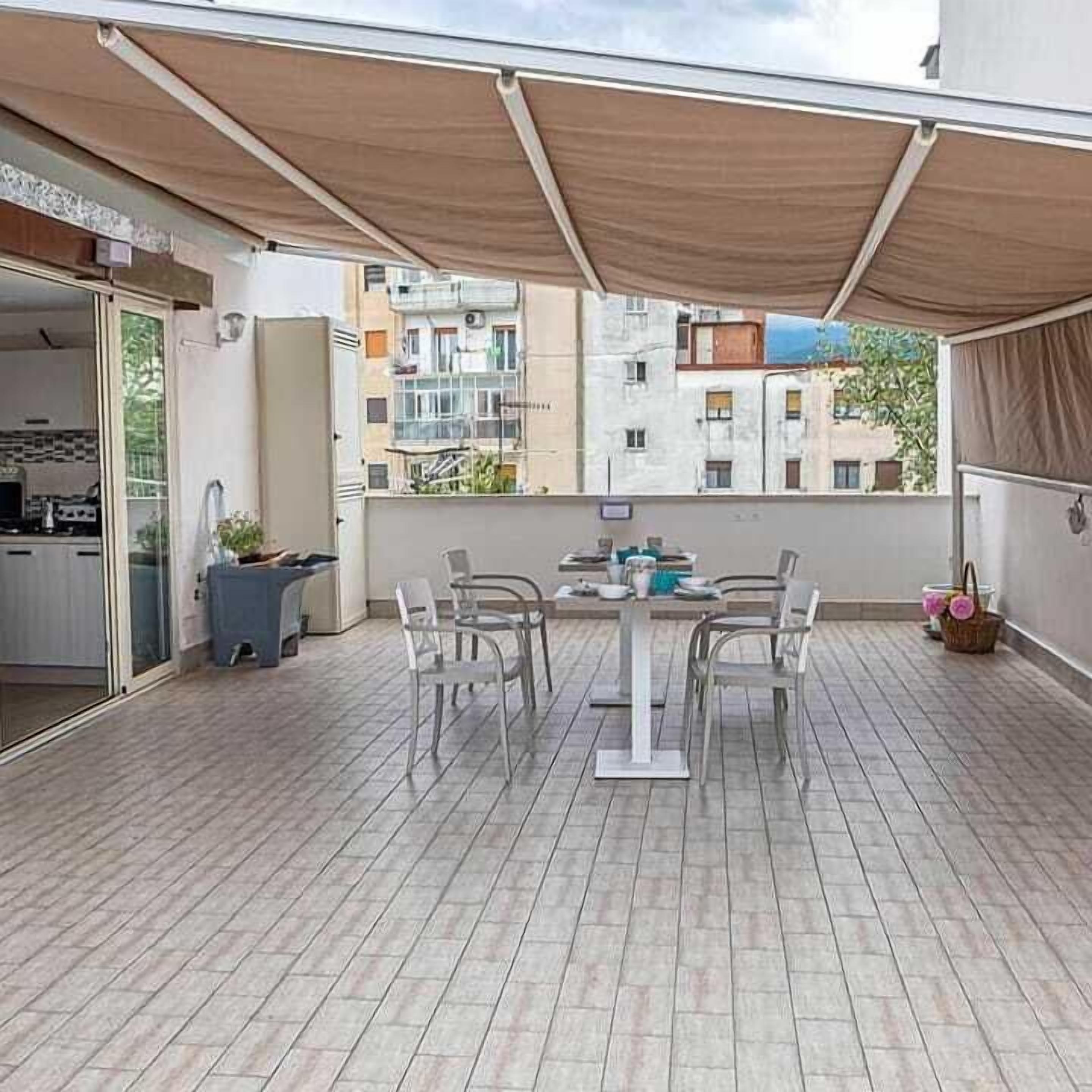 Un balcon avec une table et des chaises, une porte-fenêtre coulissante donnant sur une cuisine et une vue sur les immeubles voisins.