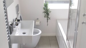 A modern bathroom with a freestanding sink, a toilet, a shower, and a window providing natural light. - Cosy Two Bed in Islington (London)