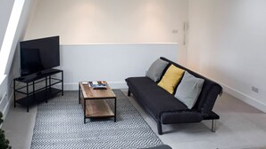 A modern living room with a black sofa, a wooden coffee table, a black TV stand, and patterned rugs. - Cosy Two Bed in Islington (London)