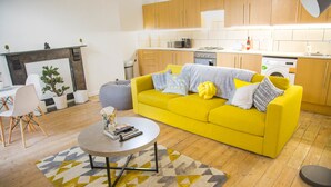 Een moderne woonkamer met een gele bank, een ronde salontafel en een open haard.