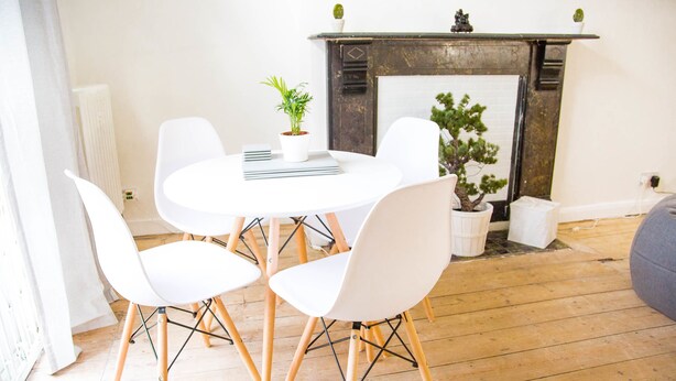 Een eethoek met een ronde tafel, witte stoelen en een potplant.