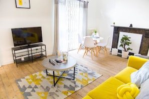 Una sala de estar con televisión, una mesa redonda de centro, un sofá amarillo y una chimenea.