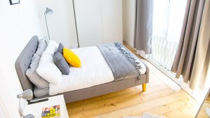 Een slaapkamer met een bed, nachtkastje, lamp en uitzicht op het exterieur.