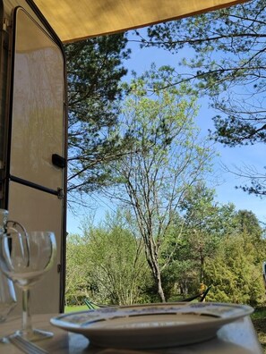A view through an open tent door with a table set for dining, featuring a clear view of trees and a blue sky. - Camping des vignes (Dun)