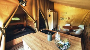 A cozy tented accommodation with a bed, a table with a kettle, a chair, and a small dining area. - Camping des vignes (Dun)