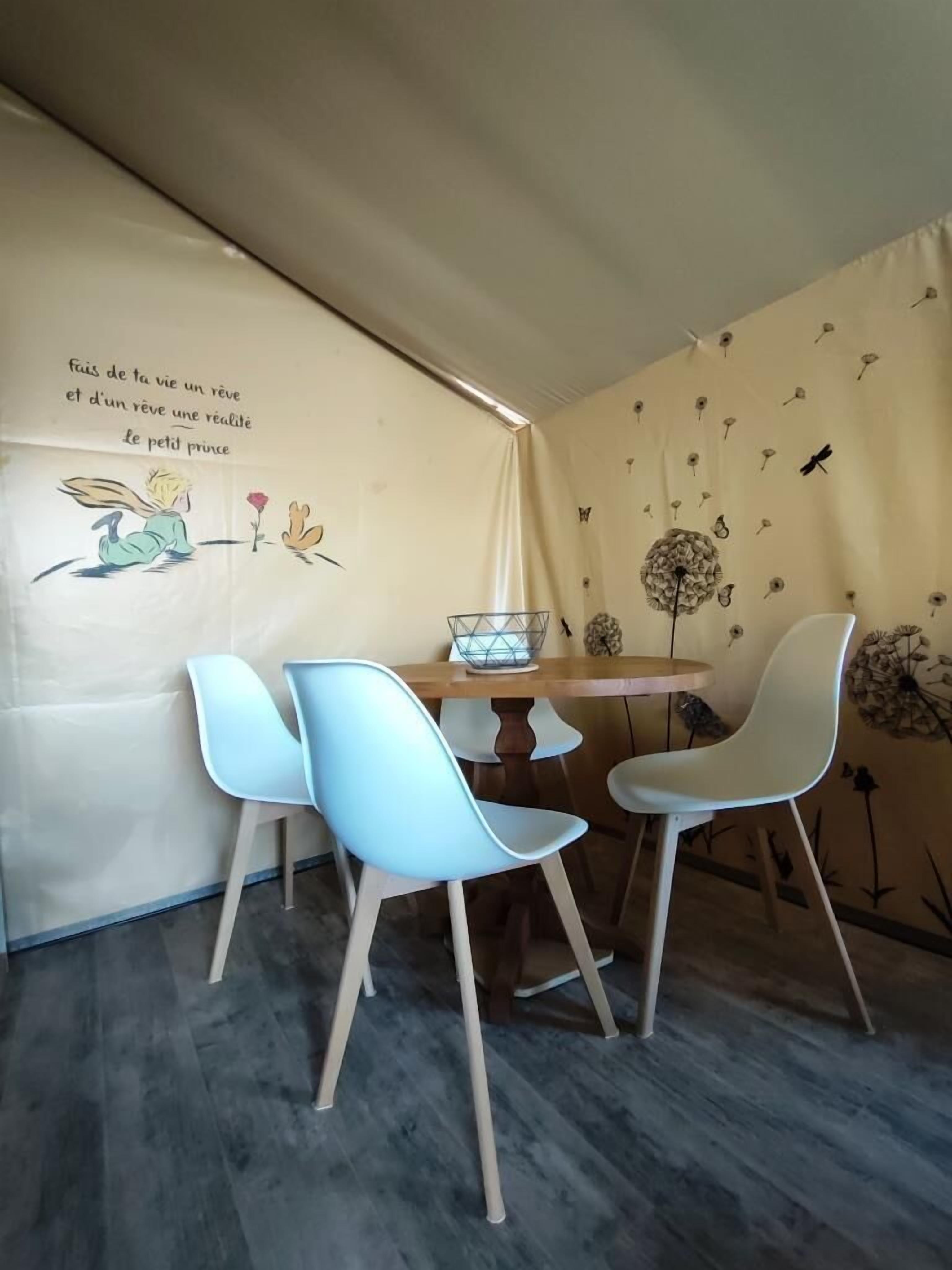 Een eetruimte met een tafel en stoelen, een muur met een citaat en een tekening, en een muur met een patroon.