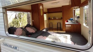A caravan interior with a bed, a kitchenette, and a small seating area. - Camping des vignes (Dun)
