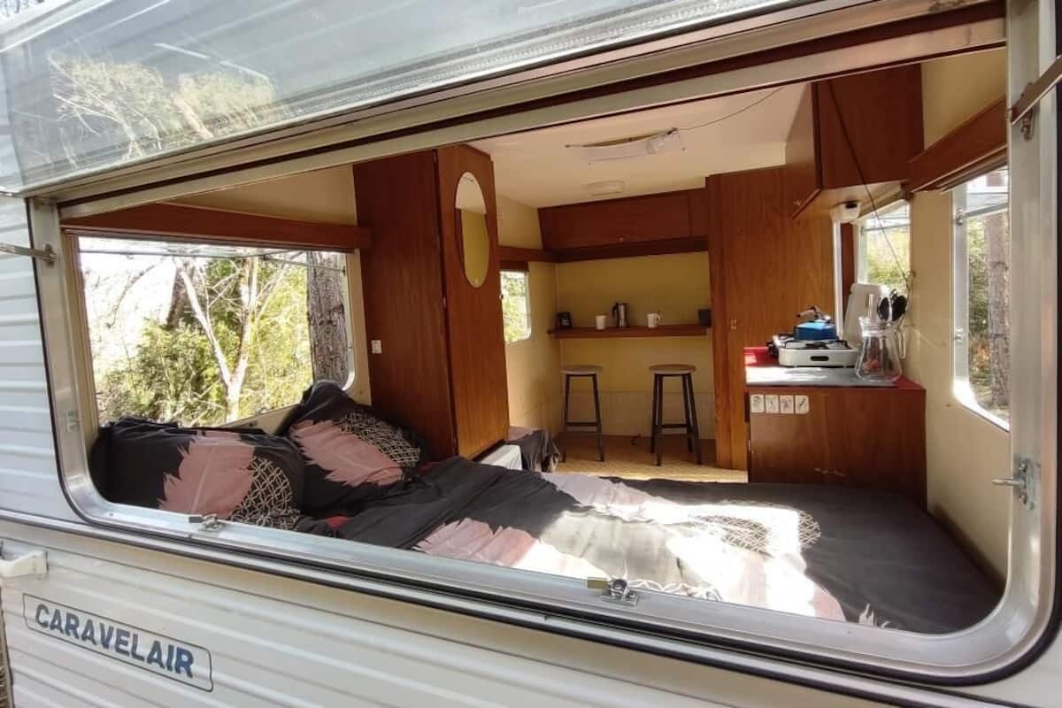 Interior de una caravana con cama, kitchenette y una pequeña zona de estar.