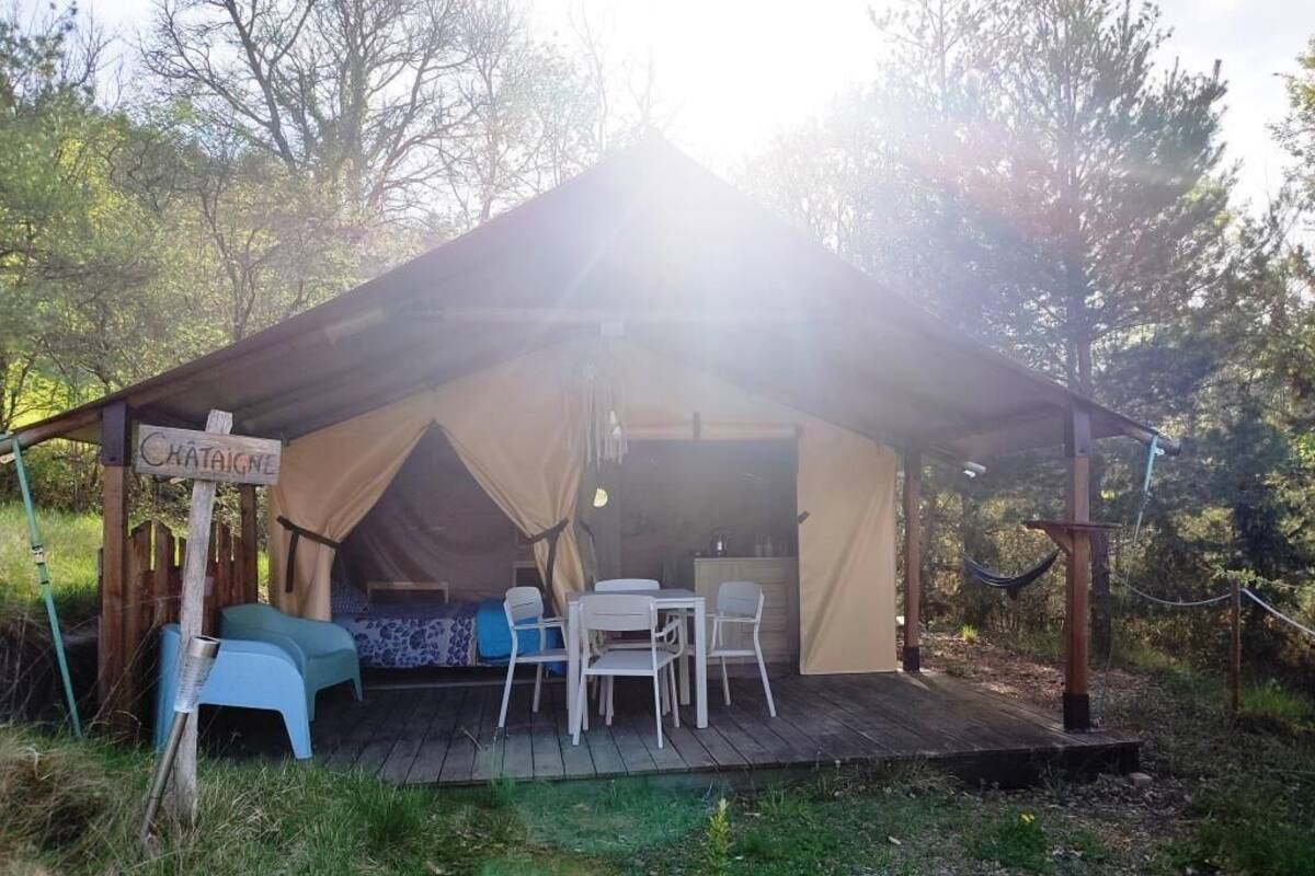 Alojamiento en tienda de campaña con un letrero que dice "Chataigne", una terraza de madera y una mesa con sillas.