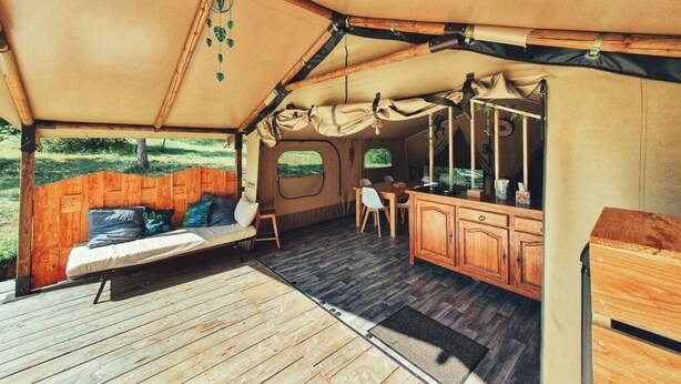 A tented accommodation with a wooden deck, a bed, a small table, and a kitchenette. - Camping des vignes (Dun)