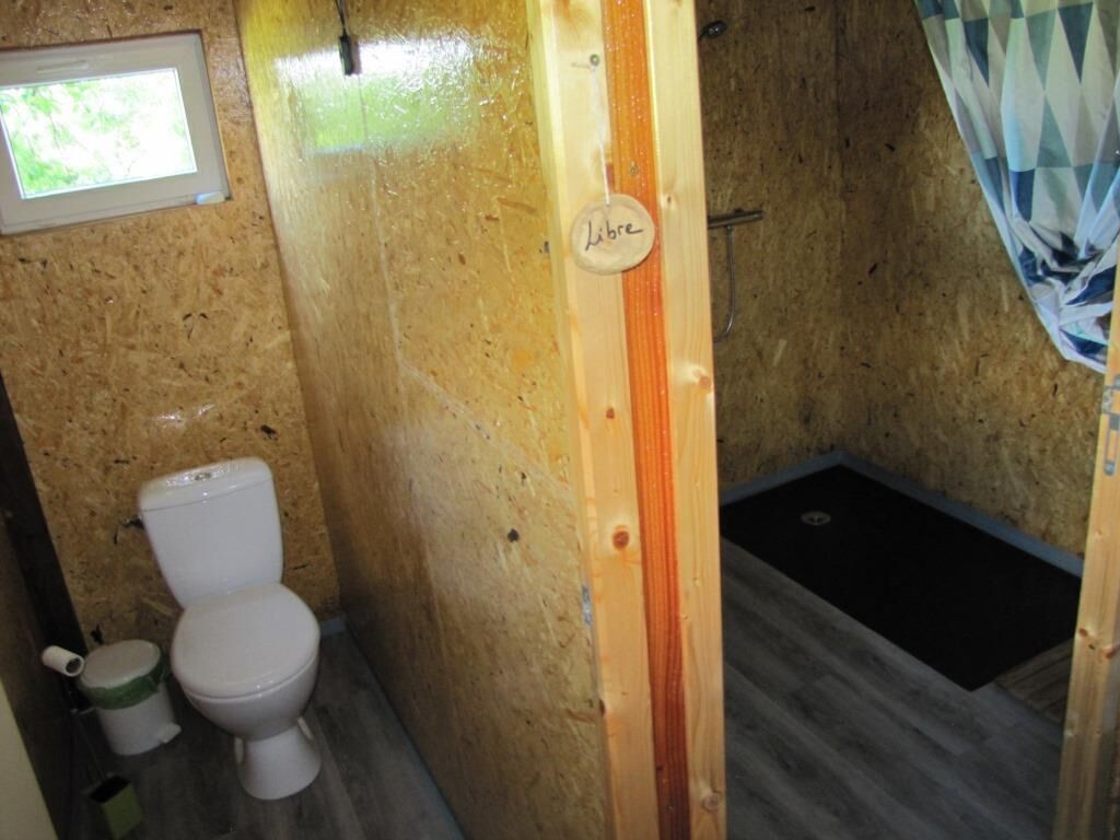 Une petite salle de bain compacte, comprenant des toilettes, un espace douche et une cloison en bois portant l'inscription « Occupé ».