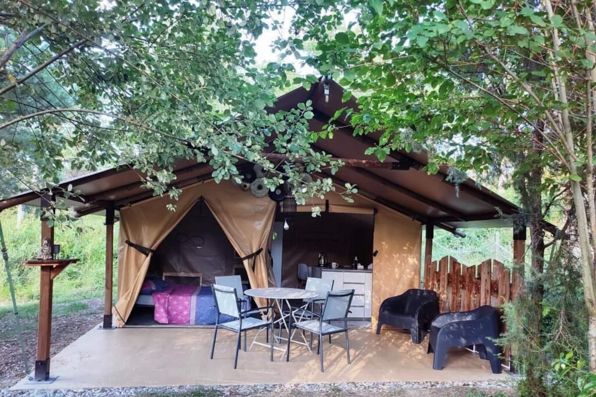 Una tienda de campaña rústica al aire libre con una zona de cocina, una mesa de comedor y sillas.