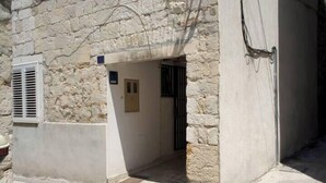 A stone building with a narrow entrance, a small door, and a window with shutters. - Rooms Radunica street (Split)
