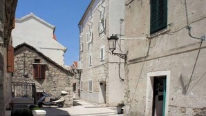 A narrow street with stone buildings, a scooter parked on the side, and a clear blue sky. - Rooms Radunica street (Split)